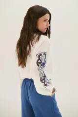 Camisa blanca de manga larga con bordados florales marrones en las mangas.