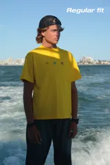 Camiseta celeste de manga corta con cuello redondo y estampado frontal de tres recipientes con cereales. En la parte trasera tiene un estampado grande con el texto "iUTTAi STARS" y un plato con cereales.