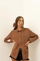 Camisa marrón de corte recto con cuello camisero, cierre frontal con botones, mangas largas con puños abotonados y bolsillos de parche en el pecho.