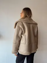 Campera gamulan color beige con interior de piel sintética, cuello solapa y cierre con botones a presión.
