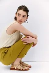 Pantalón babucha de tiro alto confeccionado en símil lino color verde oliva. Tiene calce relajado que ajusta hacia el ruedo y largo hasta los tobillos, la cintura es elastizada y cuenta con 6 presillas y lazo de ajuste en la misma tela. Tiene bolsillos diagonales en laterales y dos bolsillos ojal falsos en espalda.