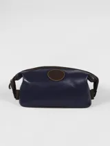 Neceser de cuero color azul marino con detalles y pespuntes en cuero marrón. Presenta un parche circular con logo grabado en el frente y cierre superior con cremallera.