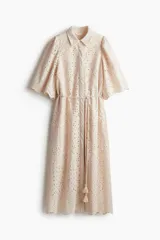 Vestido midi color beige con broderie, cuello camisero, botones ocultos, mangas abullonadas al codo, cinturón fino con borlas y ribete festoneado.