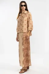 Camisa color beige con estampado de flores y rayas verticales marrones, de manga larga con puños elastizados y lazos regulables en los costados del ruedo.