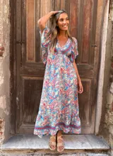 Vestido largo con estampado paisley en tonos celeste, rojo y beige. Tiene escote en V, mangas cortas con volantes y corte imperio.