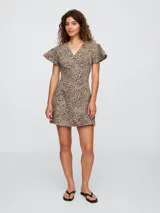 Vestido corto de denim con estampado de leopardo, corte entallado y falda acampanada. Tiene cuello en V, mangas cortas con volados y cierre frontal con botones.