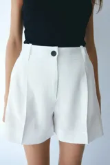 Short blanco de corte sastrero con cierre y botón, bolsillos al bies y bolsillo trasero decorativo. Piernas con pinzas y pliegues adelante y atrás.