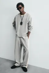 Pantalón de jogging gris con corte relaxed fit, cintura elástica ajustable con cordón interior, bolsillos laterales y traseros de vivo, y banda lateral color crema.