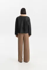 Campera corta de efecto cuero negro, con forro y cuello de corderito color beige. Cierre frontal mediante botones y bolsillos amplios.