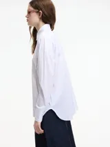 Camisa blanca de algodón con cuello camisero, cierre frontal con botones y apliques de cadenas plateadas.