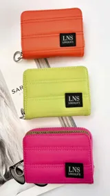 Billetera corta con cierre alrededor y tapa, confeccionada en tela capitoneada. Incluye varias reparticiones con tarjeteros y bolsillos internos, y una correa de mano desmontable. Disponible en negro, rojo y dorado.