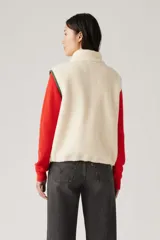 Chaleco color crema de sherpa con cuello alto, cierre frontal con cremallera y ribete de contraste en verde.