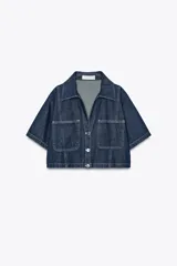 Camisa corta de denim azul con cuello solapa, escote pico, manga corta, bolsillos delanteros de plastrón y cierre frontal con botones metálicos.
