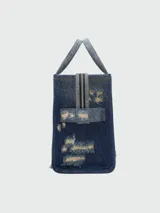 Bolso tote Marc Jacobs de tamaño mediano confeccionado en denim azul con efecto desgastado. Presenta el logo "THE TOTE BAG MARC JACOBS" estampado en blanco en el frente, doble asa corta superior y correa bandolera extraíble de tela negra.