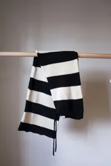 Bufanda larga tejida a rayas horizontales anchas en color blanco y negro, con terminación desflecada y cordones finos en los extremos.