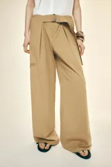 Pantalón color beige de tiro alto con cinturón ajustable con hebilla metálica. Presenta bolsillos laterales, de vivo en la pierna y de parche en la espalda.