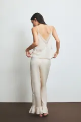Conjunto de pijama color crema con detalles de encaje en el top. El top es de tirantes finos y el pantalón es largo con volados en el ruedo.