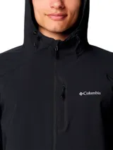 Chaqueta tipo softshell con capucha, color negro, cierre frontal completo y logo de Columbia bordado en el pecho izquierdo. Presenta puños elásticos y un dobladillo trasero más largo para mayor cobertura.