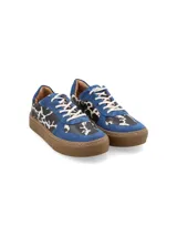 Zapatillas bajas con estampado de vaca en blanco y negro, detalles en gamuza azul y suela marrón.