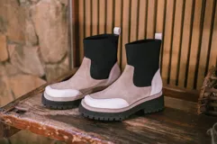 Bota de cuero color beige con caña de neopreno negra, suela track color negro y tirador trasero.