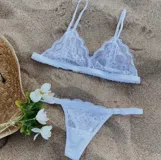 Conjunto de lencería blanco de encaje, compuesto por un corpiño tipo bralette con breteles regulables y una tanga regulable con elásticos anchos y corte cola less.
