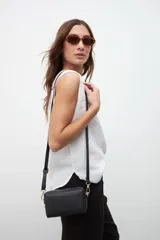 Bandolera negra con correa larga regulable, cierre superior y herrajes dorados.