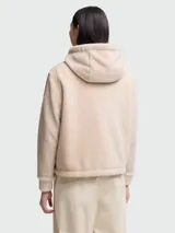 Buzo con capucha de tejido afelpado color beige claro, con cierre frontal de cremallera y bolsillos canguro. Presenta puños y bajo acanalados.