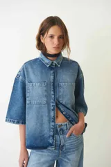 Camisa de jean celeste de manga corta, con dos bolsillos frontales, abotonada con broches a presión y cuello camisero.