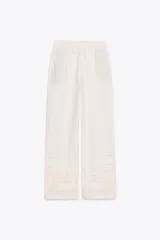 Pantalón de tiro medio color crudo, confeccionado en mezcla de algodón y lino, con cintura elástica ajustable con cordones, bolsillos laterales ocultos y detalle de bordados perforados a tono en el ruedo.
