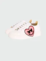 Zapatillas bajas de cuero blanco con aplique de parche bordado de cara sonriente amarilla con relámpagos en los ojos y dedo medio levantado.
