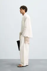 Camisa de corte relajado, color blanco hueso, con finas rayas verticales en tono grisáceo. Presenta cuello solapa, manga larga, bolsillo de parche en el pecho y bajo con aberturas laterales.