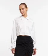 Camisa blanca corta de satín con cuello alto, manga larga con lazo en los puños, abotonada en el frente y abertura en la espalda.