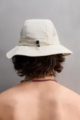 Sombrero tipo bucket color beige, confeccionado en tejido técnico con perforaciones en la copa para mejorar la transpirabilidad. Tiene ajuste elástico y ala ancha con pespuntes.