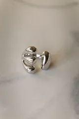 Anillo plateado de acero quirúrgico hipoalergénico con diseño abierto y tres gotas en un extremo y una gota en el otro.