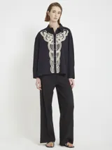 Camisa negra de corte amplio con botones en la parte delantera y aplique de macramé en el frente.