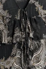 Vestido corto negro con estampado paisley en tonos beige y detalles dorados. Escote en V con lazos ajustables, mangas largas con puños elásticos y volantes en el mismo tejido en el escote y el ruedo.