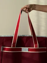 Bolso tipo tote de neopreno color negro y marrón, con cierre superior, bolsillo frontal marrón con logo rojo, bolsillo interno y externo con cierre, doble asa de mano marrón con detalles blancos y opción de correa larga.