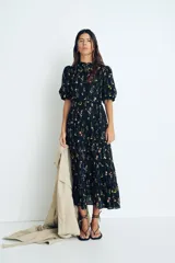 Vestido largo de algodón negro con estampado de flores pequeñas en tonos rosa y amarillo. Tiene cuello mao, mangas globo cortas, cinturón fino extraíble y falda acampanada con fruncido escalonado.