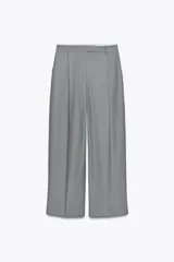 Pantalón gris de tiro alto con bolsillos delanteros, pierna ancha y cierre frontal con cremallera y ganchos metálicos.