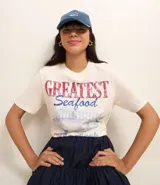 Remera t-shirt de algodón color crema, con cuello redondo y mangas cortas. Estampa frontal con la frase "Greatest Seafood" y un dibujo de un pez.