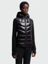 Chaqueta híbrida negra de Moncler, con cuerpo acolchado brillante y mangas de tejido de punto liso. Cuenta con capucha ajustable y cierre frontal de cremallera.