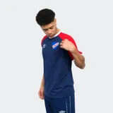 Remera de algodón blanca con mangas cortas ranglan azul marino con una franja roja en el hombro. Tiene el logo de Umbro bordado en el pecho y el escudo del Club Nacional de Football.