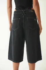 Bermuda de denim negro con tachas redondas plateadas, tiro bajo, cuatro bolsillos, pasacintos y cierre con botón metálico.