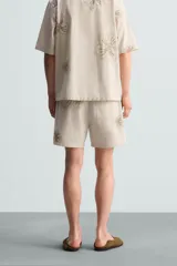 Bermuda regular fit color beige con bordados de flores en tono marrón. Tiene cintura elástica ajustable con cordón, bolsillos laterales y un bolsillo trasero de plastrón.