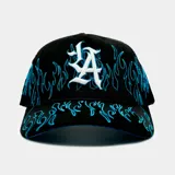 Gorro estilo trucker negro con paneles traseros de malla. Presenta un bordado frontal de una letra 'A' estilizada en blanco y contornos de llamas bordadas en azul brillante alrededor del frente y la visera.