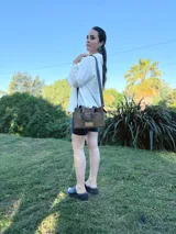 Cartera bandolera de cuero color verde oliva, con forro de tela, bolsillo delantero con cierre y bolsillo interno. Tiene correa larga regulable y manijas cortas.