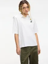 Remera tipo polo blanca de manga corta con hombreras y pins removibles en la delantera.