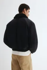 Campera bomber de nylon color negro con corte holgado y levemente acolchada. Cuenta con cuello de peluche al tono, cierre frontal metálico, bolsillos laterales con solapa y un bolsillo con cierre en la manga. Posee puños y bajo acanalados.