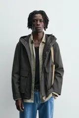 Parka relaxed fit color negro confeccionada en tejido de lino que repele el agua. Tiene cuello con capucha ajustable, mangas largas con puños abotonados, bolsillos frontales con solapa y cierre frontal con cremallera oculta por solapa con botones a presión.