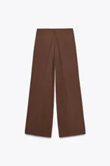 Pantalón color ladrillo de tiro medio con trabillas, detalle de pliegues, bolsillos laterales y falsos bolsillos de vivo en la espalda. Cierre frontal con cremallera y botón.
